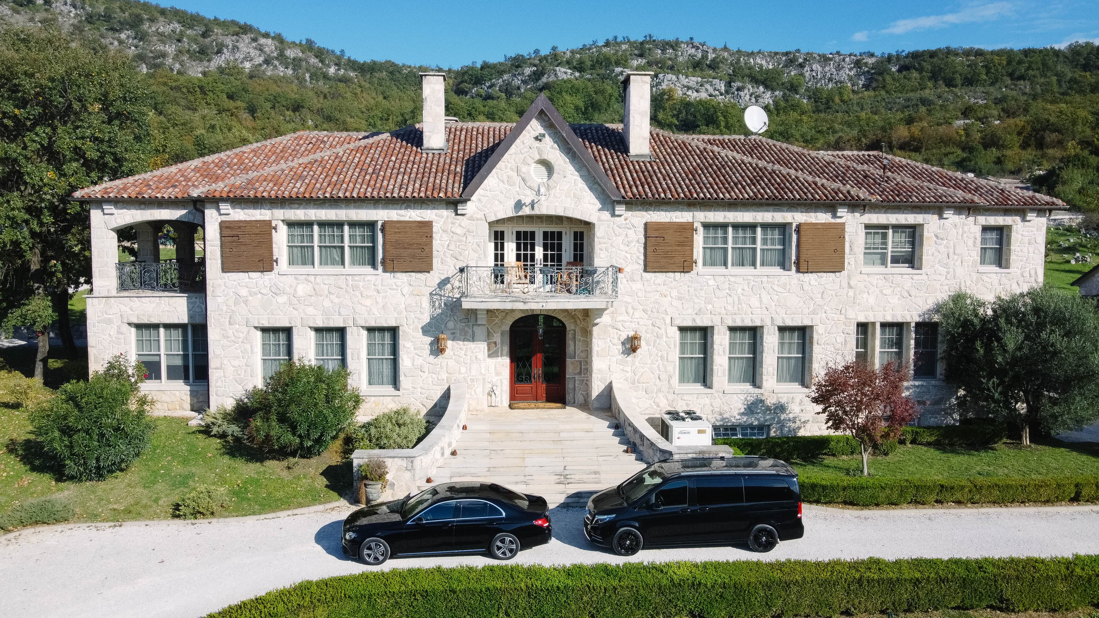 Black Mercedes-Benz sedan and van parked in front of a large stone house