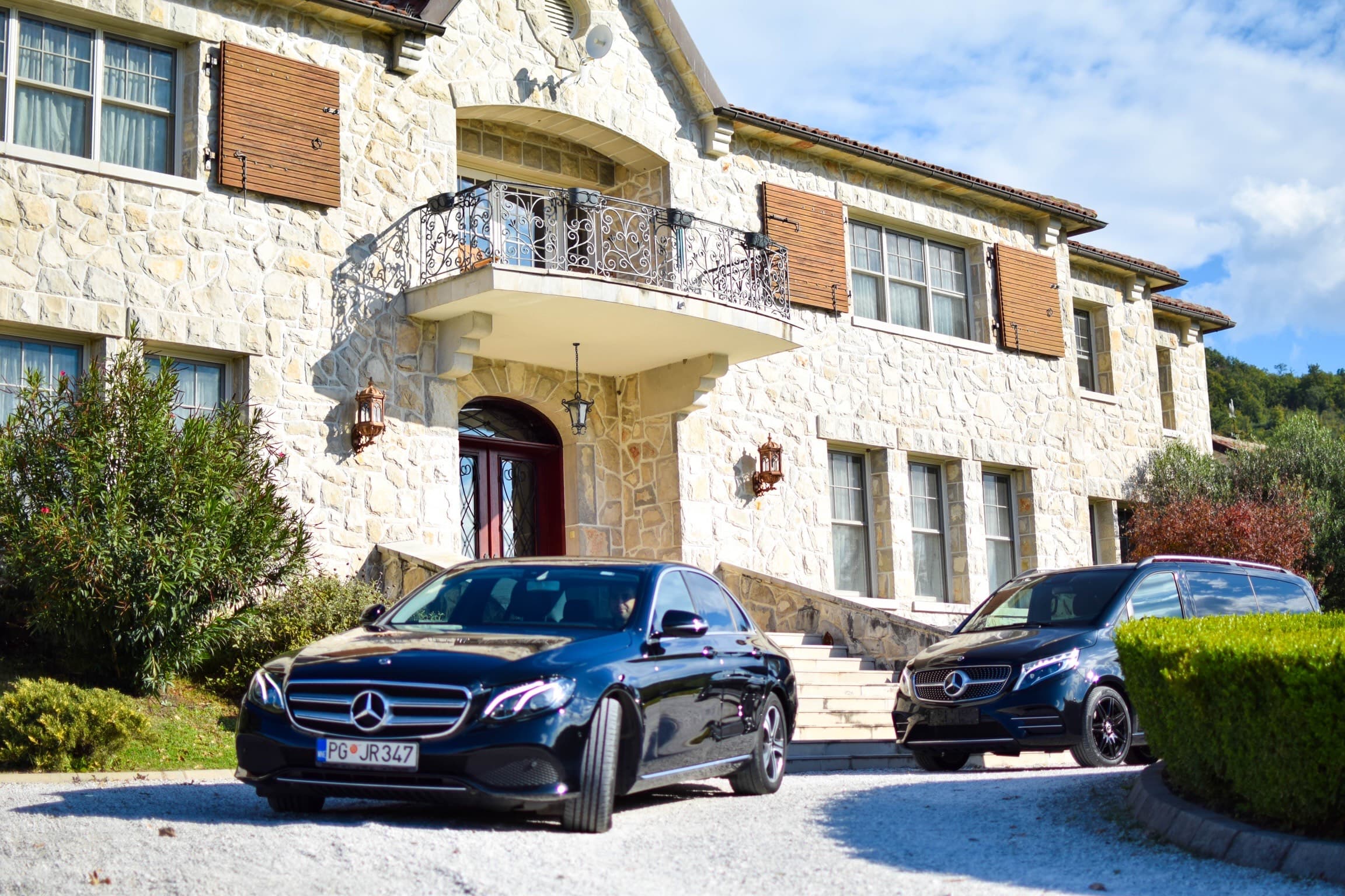 Black Mercedes-Benz sedan and van parked in front of a stone house with a balcony